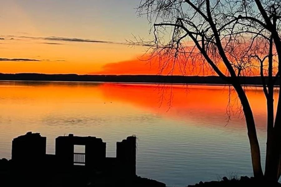 橙色和黄色的夕阳投射在水面上，建筑物和树木在前景中可见.